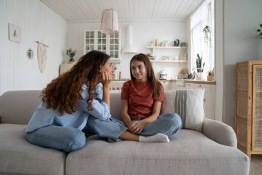 Genç kız, sevgi dolu, destekleyici bir anneyle sırlarını paylaşıyor, anne-baba, ergen bir kızla sohbet ediyor, evde kanepede yan yana oturuyor. Sağlıklı ebeveyn-genç ilişkileri