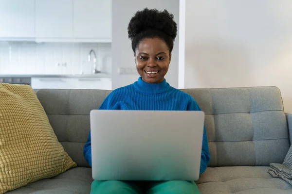 stock image Successful African American woman freelancer smiling working from home doing order using laptop. Happy girl employee of online company makes career as online journalist or copywriter sits on couch