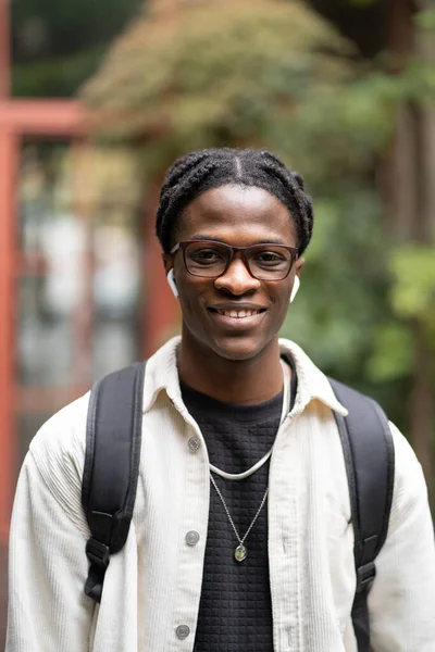 stock image Portrait of cheerful African millennial guy student in glasses smiling at camera, standing near university campus outdoors. Happy young black man with backpack, enjoying college life. Selective focus