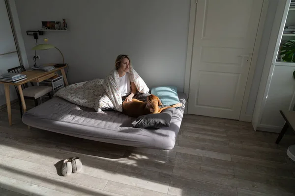 stock image Middle-aged woman sitting on bed with dog in morning at home, single lady enjoying living alone with beloved pet, sharing life with furry friend. Pet ownership and mental health, companion animals