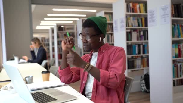 積極的な社交アフリカ人の男性は ラップトップを使用してビデオ通話で話して笑顔大学図書館に座っています 陽気幸せな黒人男性学生ビデオチャットでのプレゼンテーションや論文の詳細を議論 — ストック動画