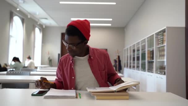 Çalışmalara Odaklanmamış Afrikalı Amerikalı Erkek Öğrenci Kütüphanede Oturmuş Sınav Kitaplarına — Stok video