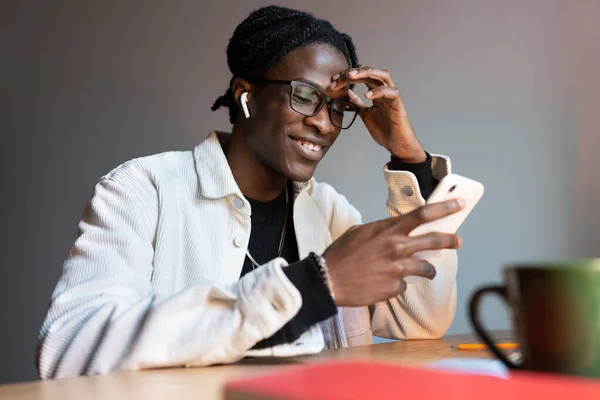 成功した笑顔アフリカ系アメリカ人男性携帯電話を保持することは面白いモバイルアプリやソーシャルメディアを使用しています 陽気な若いです黒男とともにスマートフォン座って室内で音楽を聴きますヘッドフォン — ストック写真
