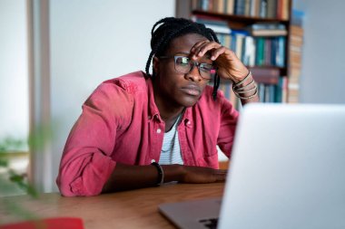 Sıkıcı genç Afrikalı serbest çalışan Laptop ekranına bakarak konsantre olamıyor. Evden uzakta çalışırken motivasyonunu kaybeden üzgün bir zenci işe karşı ilgisiz hisseder.