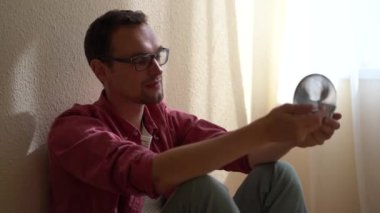 Young relaxed man sitting on floor playing with anti-stress metal spring toy for calmness and smiling, distracting from negative thoughts. Fun home activities, stress relief concept