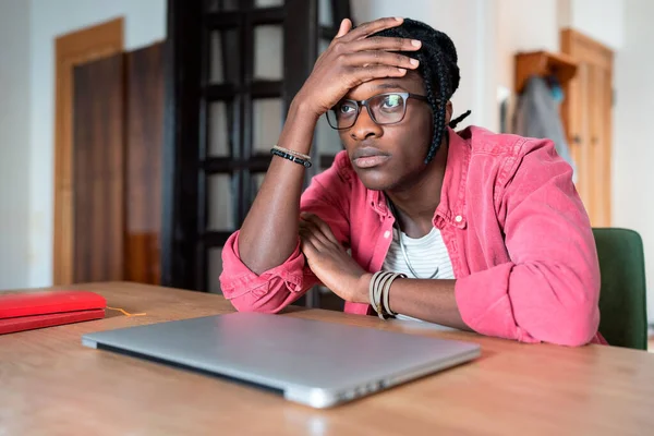 Young stressed sad African student guy sitting at table with closed laptop feeling lazy and unmotivated to study from home, lack of motivation in online learning. Freelance burnout concept