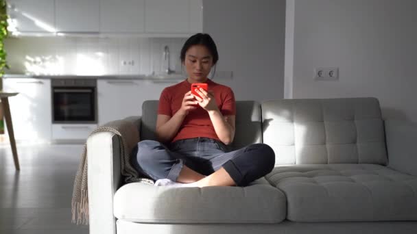 インターネットの接続が遅いことに悩まされているスマートフォン感覚を使用してソファの上に座って神経質な怒っているアジアの女性 不幸な韓国の女の子は不快なニュースを取得し 携帯電話を捨てる ストレスを感じて — ストック動画
