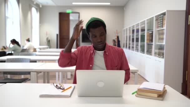大学で講義の準備をしているアフリカ系アメリカ人の男性がノートパソコンや本を持ってテーブルに座って困惑しました 疲れました男学生終了タイプエッセイとRus目とともに指 — ストック動画