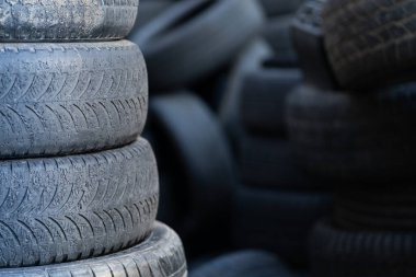 Closeup of old used rubber tires stacked with high piles, blurred background and copy space. Tyre dump. Hazardous waste requiring recycling and disposal. 