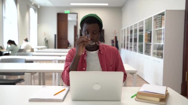 図書館で長時間勉強しながら眼鏡をはずしたりノートパソコンを閉じたりする疲れ黒い学生の男は オンライン学習に疲れ 圧倒されています Eラーニング疲労とアカデミックバーンアウト — ストック動画
