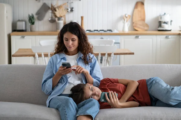 Mother and teenage daughter resting at home with electronic gadgets. Gadget addicted family mom and child using smartphones, surfing internet, watching videos. Impact of mobile devices In our life.