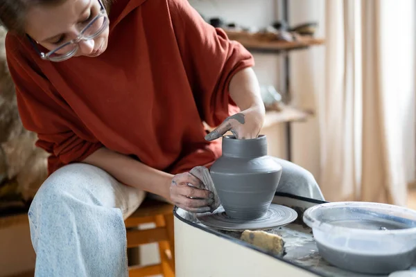 Craftswoman enjoying meditative process of making ceramics, female ceramist shaping clay on pottery wheel while working in studio, selective focus. Craft business and creative hobby concept