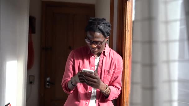Счастливый Африканский Парень Держащий Смартфон Печатающий Чаты Онлайн Стоя Окна — стоковое видео