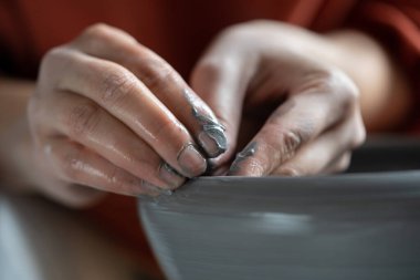 Close up of female hands molding wet clay on wheel, shaping final pottery product, potter making unique handmade stoneware, selective focus. Stress-relieving hobbies, ceramics and mental heath