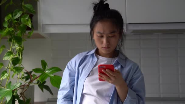 严肃的年轻亚洲女人拿着智能手机读着令人不快的信息 收到分手短信 心烦意乱的韩国女孩看着手机收到坏消息 等着男朋友的电话 — 图库视频影像