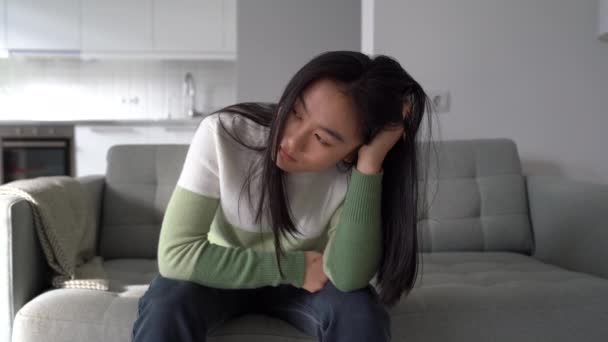 抑郁和焦虑忧心忡忡的年轻亚洲女人在失恋后感到悲伤 面对分手或离婚 焦虑地坐在沙发上的不快乐的韩国女孩 精神疾病和悲伤的概念 — 图库视频影像