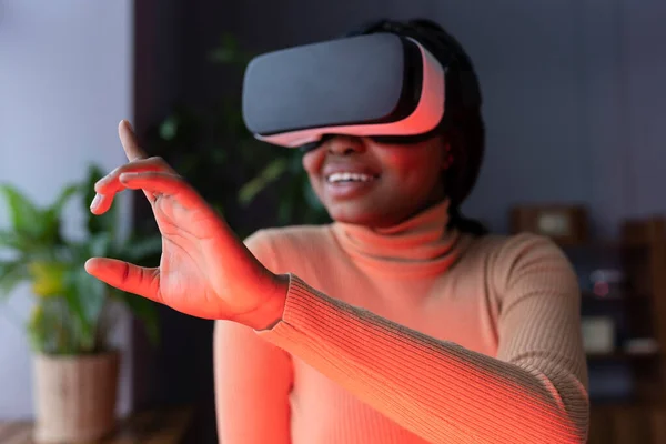 Cheerful African woman touching virtual object with finger while working in virtual reality headset, interacting with immersive digital world and testing VR technology for business. Selective focus