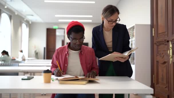 Двоє Багаторасових Студентів Навчаються Разом Бібліотеці Молоді Різноманітні Люди Сидять — стокове відео