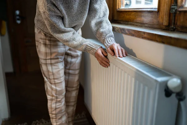 stock image Closeup of woman warming her hands on the heater at home during cold winter days, top view. Female in woolen sweater getting warm up her arms over radiator. Concept of heating season, cold weather. 