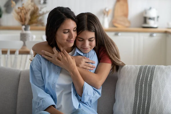 Cute girl daughter embracing mother from behind, expressing gratitude, kid telling mom she loves her. European family mommy and child cuddling, enjoying time together at home. Mother-daughter bond