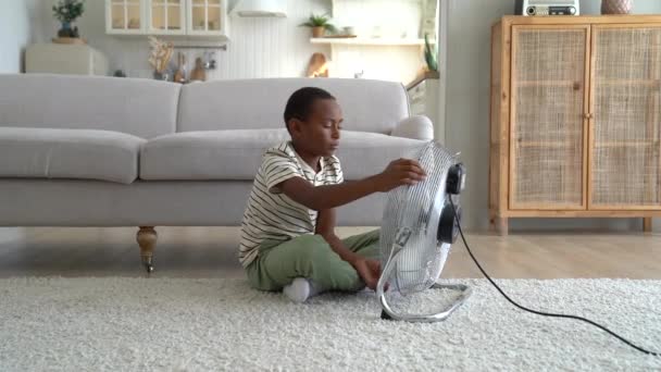 Любопытный Афроамериканец Сидит Полу Трогает Электрический Вентилятор Наслаждаясь Прохладным Свежим — стоковое видео