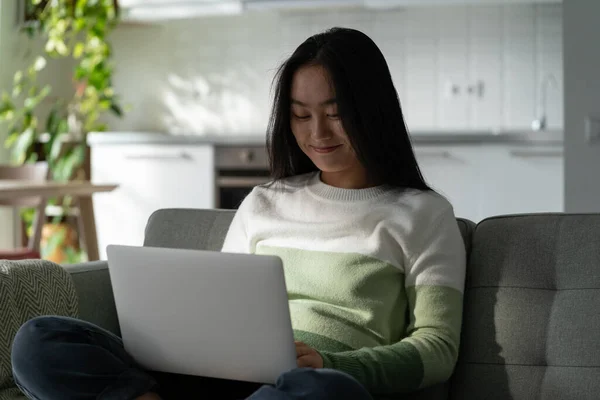 Smiling Delighted Millennial Asian Girl Sitting Sofa Home Looking Laptop — Stockfoto