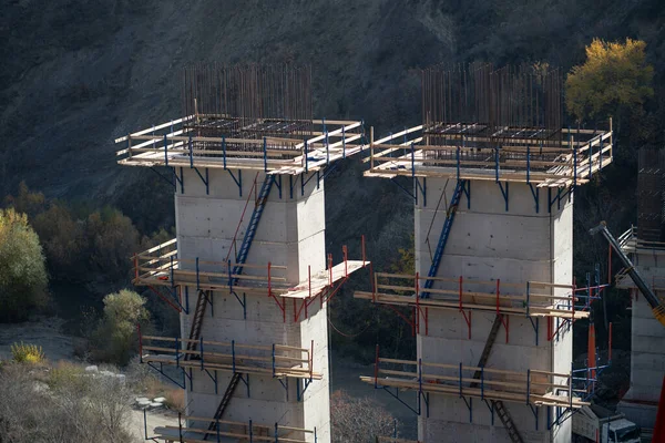 Supports of bridge under construction with wooden scaffolding and ladders for builders. Process of building transport infrastructure for railways or highways in difficult-to-reach mountainous areas