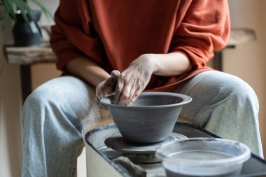 Hands of creative woman sculpture working with potter wheel during production of handmade utensils. Close-up of process of creating clay plate for serving dishes by artisan running small business 