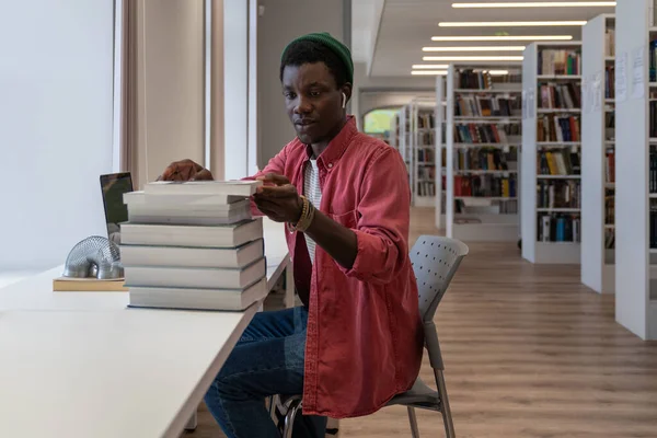 若いアフリカ系アメリカ人の学生は 研究プロジェクトのために図書館から情報を収集し 机の上に本やノートパソコンを置いています 黒人男性大学の先生はオンライン講義の準備 — ストック写真
