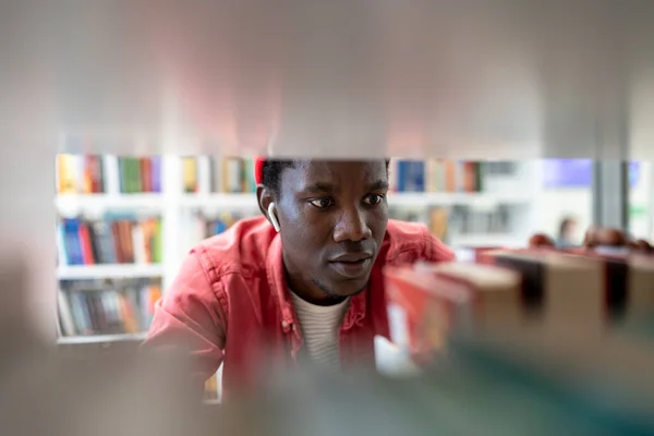 アフリカ系アメリカ人の学生が大学図書館で本を選ぶ 黒人男性は大学で学ぶ 文学テストや試験のための男性の準備 高校で民族のティーンエイジャーの研究 教育理念 — ストック写真