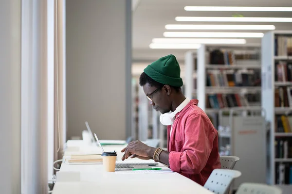焦点を当てた学生の黒人男性は 遠隔教育のための無線コンピュータを使用してノートパソコン上でオンライン試験の準備 アフリカ人は大学図書館やキャンパスで勉強している 仕事中のフリーランスの男性作家 — ストック写真