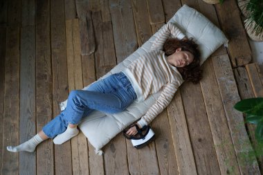Sanal gerçeklik gözlüklü kadın evde ahşap zeminde uyuyor. Sakin genç bayan rahat bir yatakta uzanıp uzun bir günün ardından sağlık ve sağlık için kestiriyor.