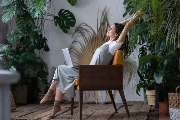 stock image Work-life balance. Happy female freelancer with closed eyes relaxing while working remotely in home garden full of exotic plants. Young woman resting during remote work at urban jungle home office