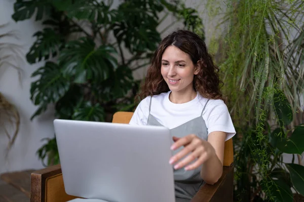 Uśmiechnięty Latynoski Ogrodnik Siedzący Fotelu Szklarni Pracujący Laptopie Otoczony Egzotycznymi — Zdjęcie stockowe