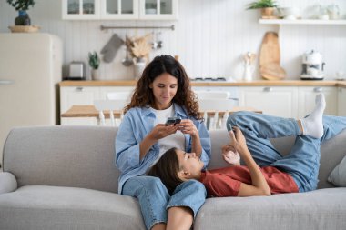 Mother and teenage daughter resting at home with electronic gadgets. Gadget addicted family mom and child using smartphones, surfing internet, watching videos. Impact of mobile devices In our life.