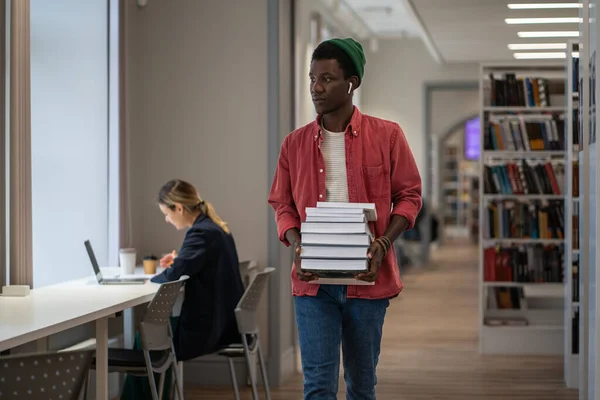 アフリカ系アメリカ人の学生が大学で効果的に勉強し 奨学金を受けるために図書館から本を借りたと考えられている 質の高い教育は読書から始まる 教科書の山を持つ男 — ストック写真
