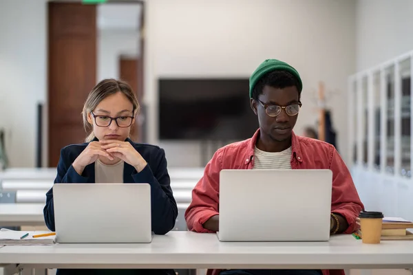 アフリカ系アメリカ人の男とメガネをかけている白人の女子学生は 大学の教室でノートパソコンの画面を見て静かに座っている 職場での研修を修了した多民族インターン — ストック写真