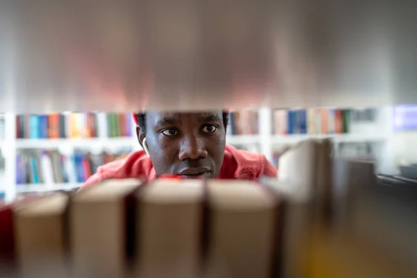 アフリカ系アメリカ人男性学生の集中的な顔を大学図書館の本棚の間に閉じます フォーカスされた黒人青年ピック文学効果的な大学研究のための書店で情報をチェック — ストック写真