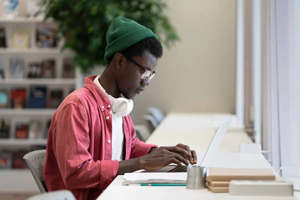 Successful professional African American guy programmer is typing code in laptop sits in comfortable office of IT company. Focused male hipster are engaged in software development or website creation