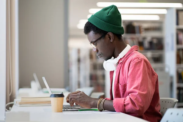 集中的に現代の大学図書館で勉強しながら ラップトップコンピュータを使用して眼鏡をかけて黒男学生 大学生は読書室でサーフィンインターネットに座って 試験の準備 — ストック写真