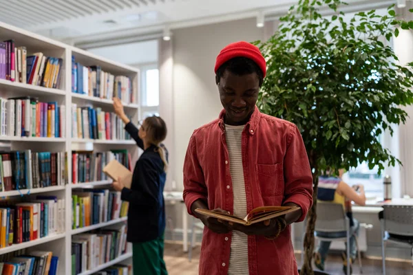 快乐的美国黑人男子站在大学校园里读书 获得了新的技能 提高了背景图书馆员的外语知识 把书正确地摆放在书架上 给学生们下订单 — 图库照片