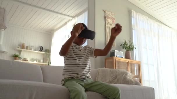 兴奋的非洲裔美国男孩一边在家里消磨时光一边享受着游戏 在虚拟现实的耳机里玩着3D赛车游戏 孩子们和沉浸在其中的技术 让孩子们欣喜若狂 — 图库视频影像