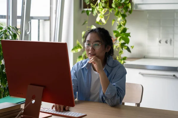 自己教育 若いアジアの女性がキッチンテーブルに座ってコンピュータでインターネット上で無料の教育リソースを探索笑顔 幸せな女の子は自宅でオンライン学習 スキルアップと再スキルの概念 — ストック写真