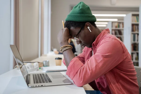 距離教育の不満 図書館のノートパソコンの前に座っているアフリカ系アメリカ人の若い男は オンライン学習で苦労し 疲れ男性学生は勉強する意欲がない感じ — ストック写真