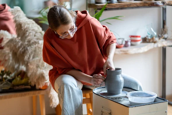 Ceramic artist woman in hoody using clay material working in potter studio. Potter master sculptor freelancer recording distance learning master class in modern workshop. Family craft small business.