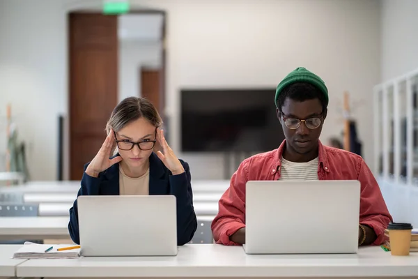 ヨーロッパの女子学生とアフリカ系アメリカ人の男性が眼鏡をかけて勉強し 教育機関の学習コースでラップトップ上のインターネット上でプロジェクトの検索情報を見る — ストック写真
