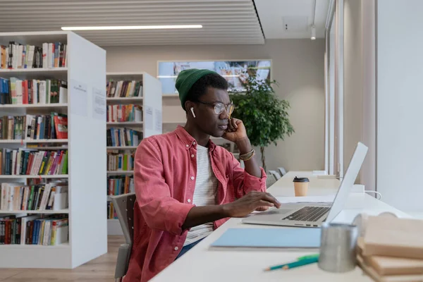 図書館でオンラインクラスの準備をしているラップトップを見ている若いアフリカ系アメリカ人の男性家庭教師に焦点を当て 教育や学習のためにコンピュータを使用して黒い男を集中させました 距離教育の概念 — ストック写真