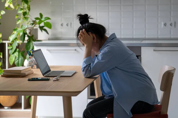 疲惫不堪的亚洲女人低着头 疲惫不堪地坐在办公桌前 拿着笔记本电脑 想着项目的最后期限是什么困难的工作任务 因国内缺乏货币债务抵押而感到沮丧的过度劳累的女性 — 图库照片