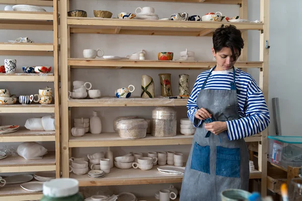 職場でエプロンを結ぶ職人は 陶芸スタジオで創造的な陶芸作品を作る粘土で作業する準備をしています 陶芸のワークショップで働くフランス人女性陶芸家 中小企業 — ストック写真