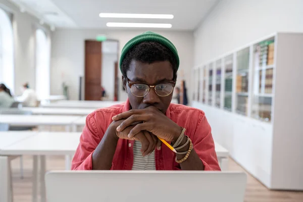 认真思考严肃的非裔美国青年自由职业者在公共图书馆的笔记本电脑上远程工作 专注于在电脑屏幕上在线阅读课本的黑人学生 远程学习 — 图库照片